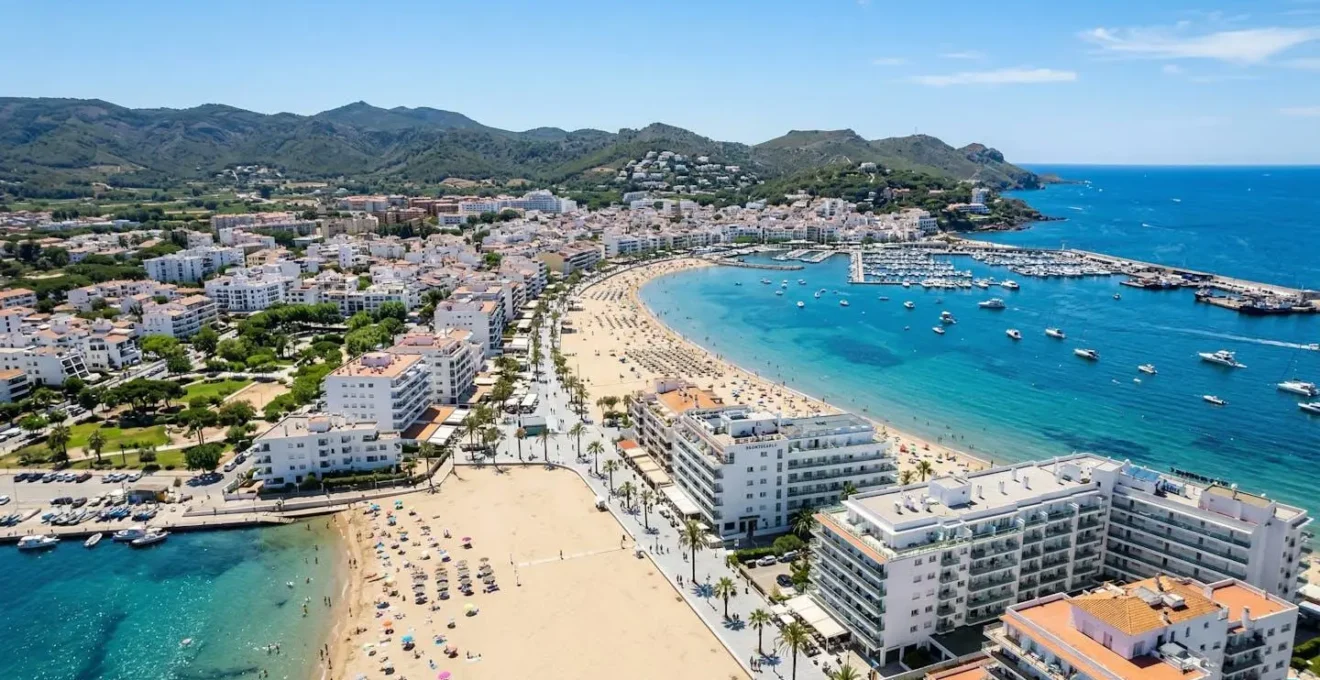 Vue aérienne du front de mer de Rosas avec immeubles résidentiels blancs modernes, baie méditerranéenne et ciel bleu dégagé